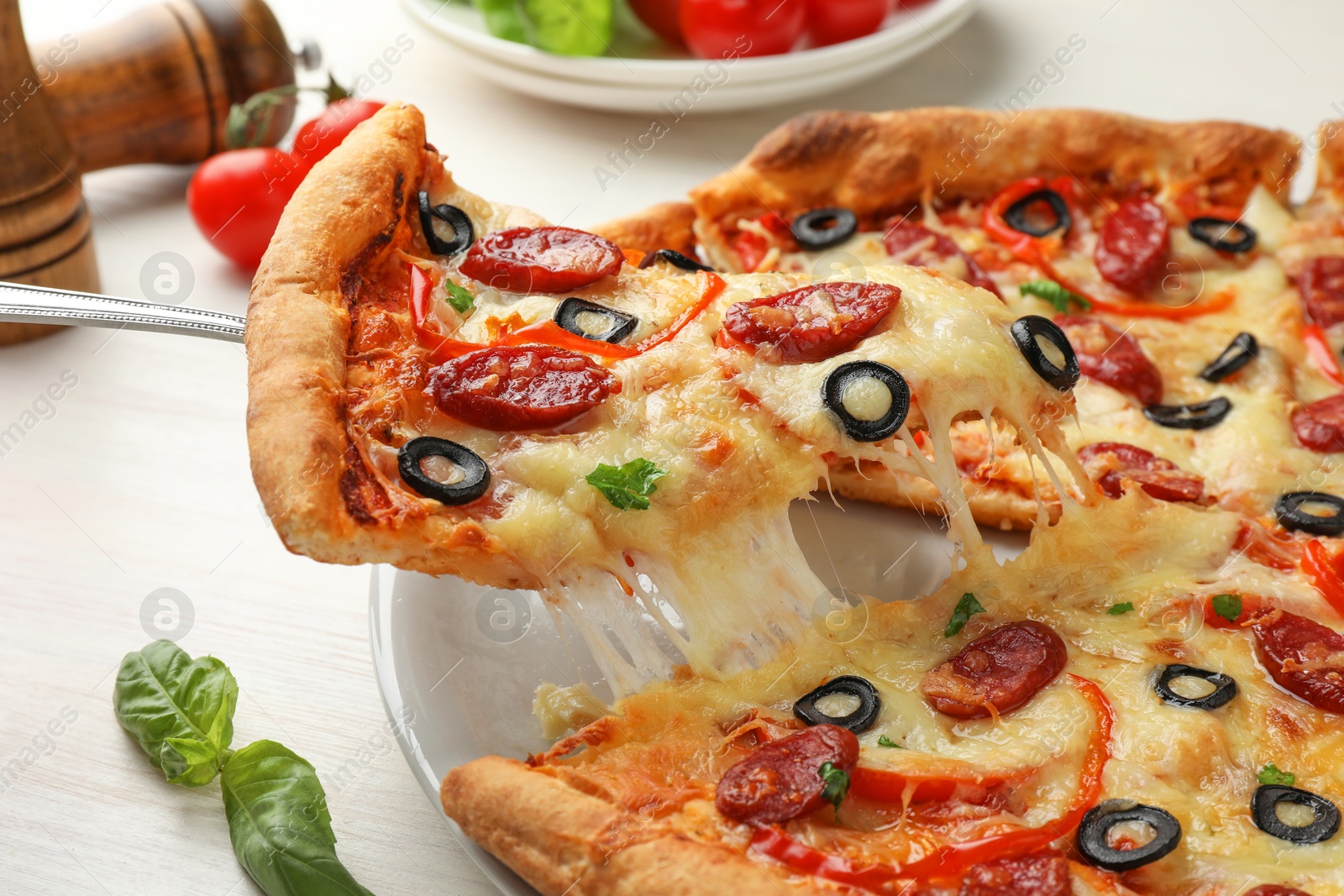 Photo of Taking piece of tasty pizza with smoked sausages, olives, pepper and parsley at light wooden table, closeup