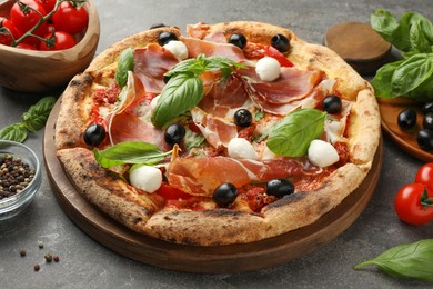 Tasty pizza with cured ham, olives, mozzarella cheese, tomatoes and arugula on gray table