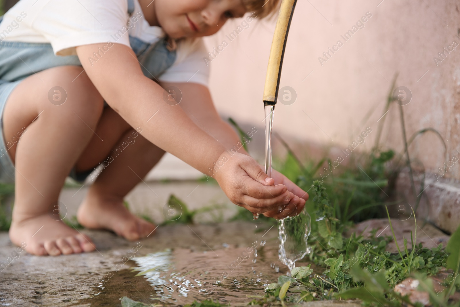 Photo of Water scarcity. Little girl drinking water from tap outdoors, closeup