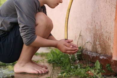 Photo of Water scarcity. Little boy drinking water from tap outdoors, closeup