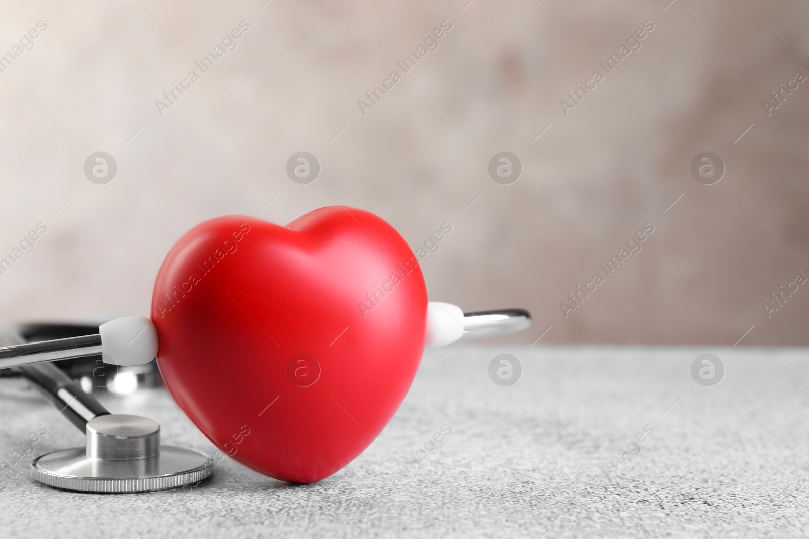 Photo of Stethoscope and red heart on grey stone table. Space for text