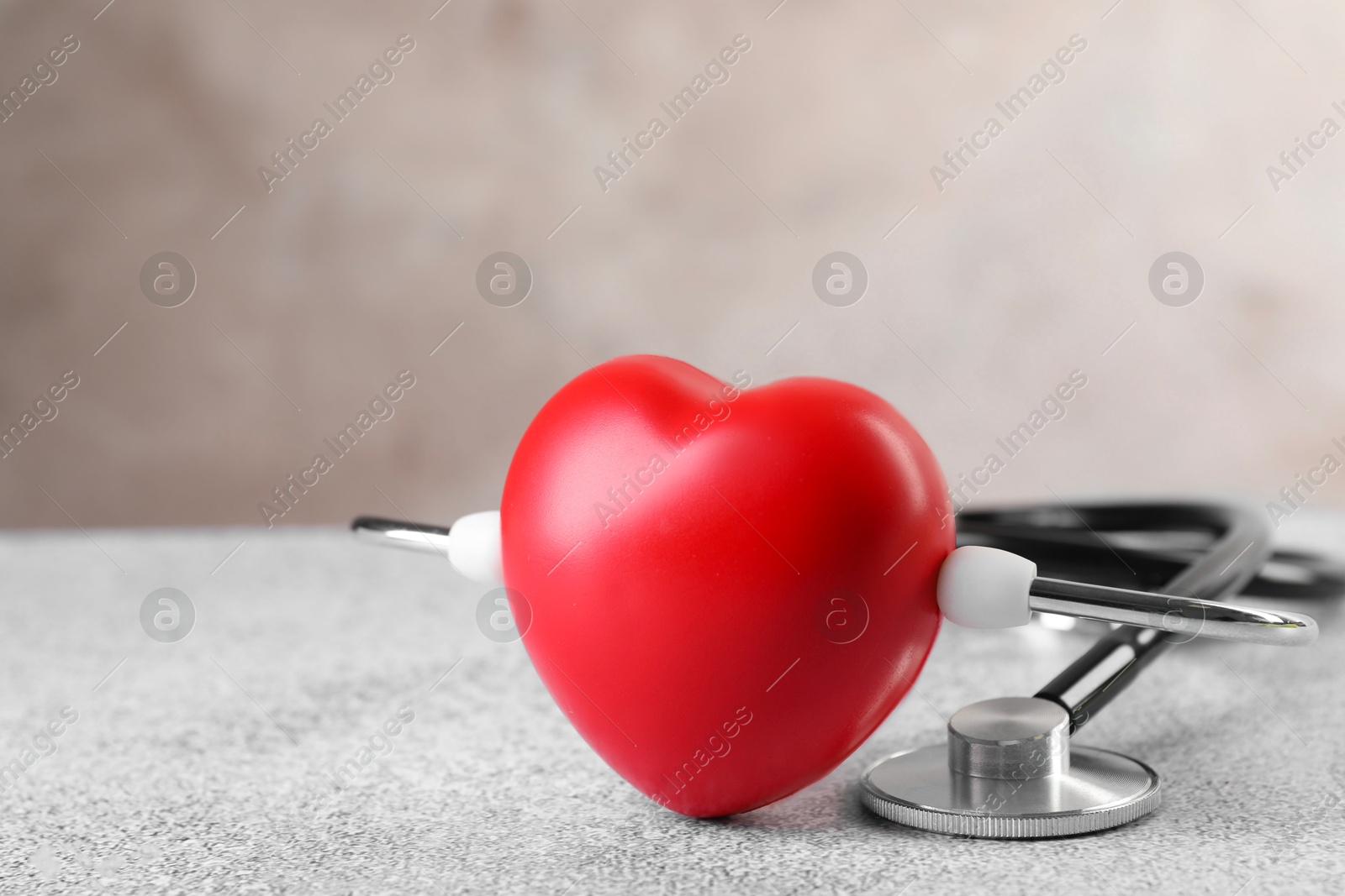 Photo of Stethoscope and red heart on grey stone table. Space for text