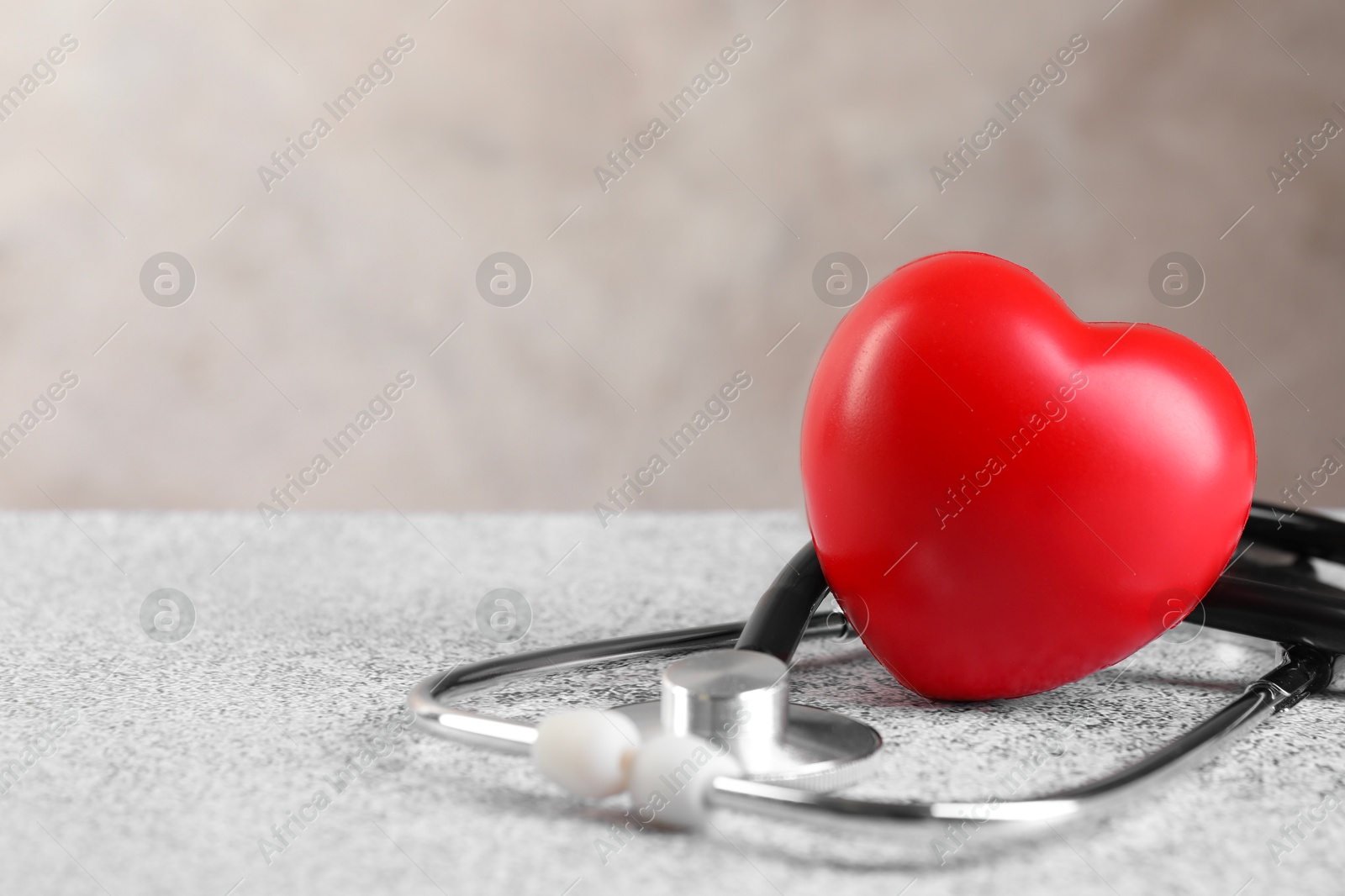 Photo of Stethoscope and red heart on grey stone table. Space for text