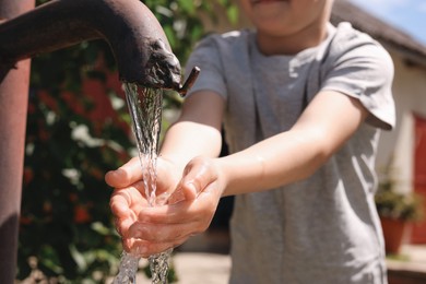 Photo of Water scarcity. Little boy drawing water with hands from tap outdoors, closeup