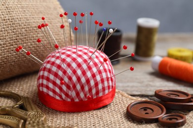 Photo of Checkered pincushion with pins and other sewing tools on wooden table, closeup