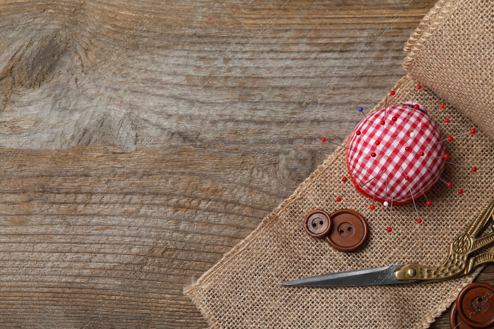 Photo of Checkered pincushion with pins and other sewing tools on wooden table, flat lay. Space for text