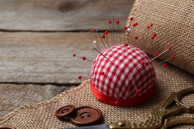 Checkered pincushion with pins and other sewing tools on wooden table. Space for text