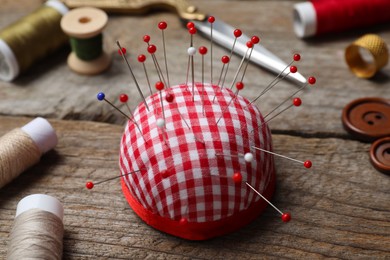 Photo of Checkered pincushion with pins and other sewing tools on wooden table, closeup