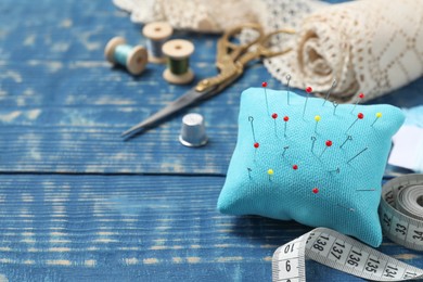 Pincushion with pins and other sewing tools on blue wooden table. Space for text