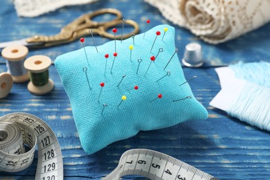 Pincushion with pins and other sewing tools on blue wooden table, closeup