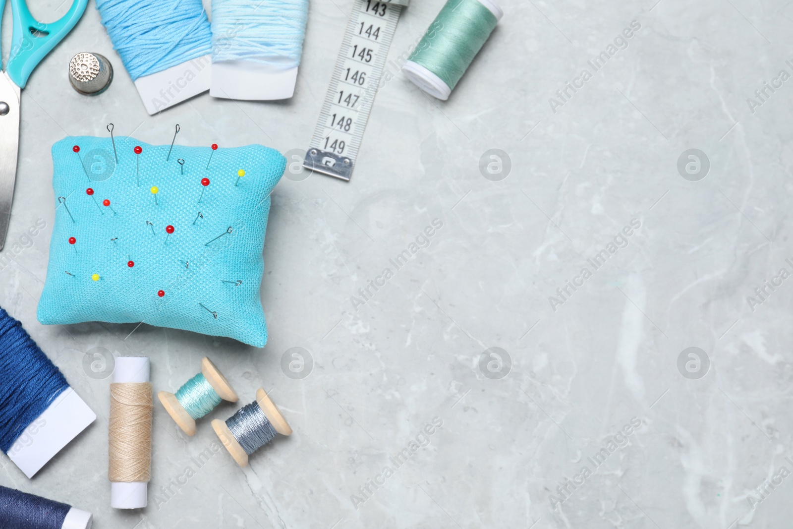 Photo of Light blue pincushion with pins and other sewing tools on grey table, flat lay. Space for text