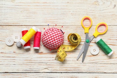 Photo of Checkered pincushion with pins and other sewing tools on light wooden table, flat lay