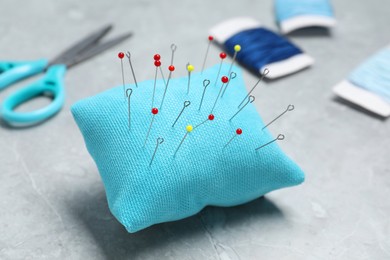 Light blue pincushion with sewing pins on grey table, closeup