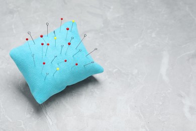 Photo of Light blue pincushion with sewing pins on grey table. Space for text