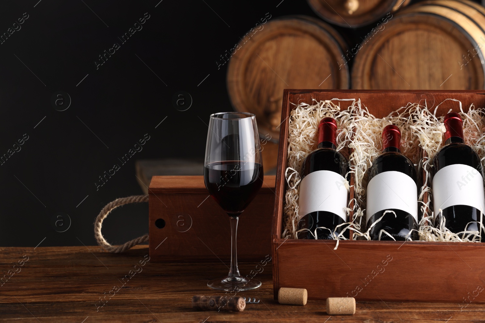 Photo of Wooden boxes, glass, corkscrew and wine bottles on table against black background. Space for text