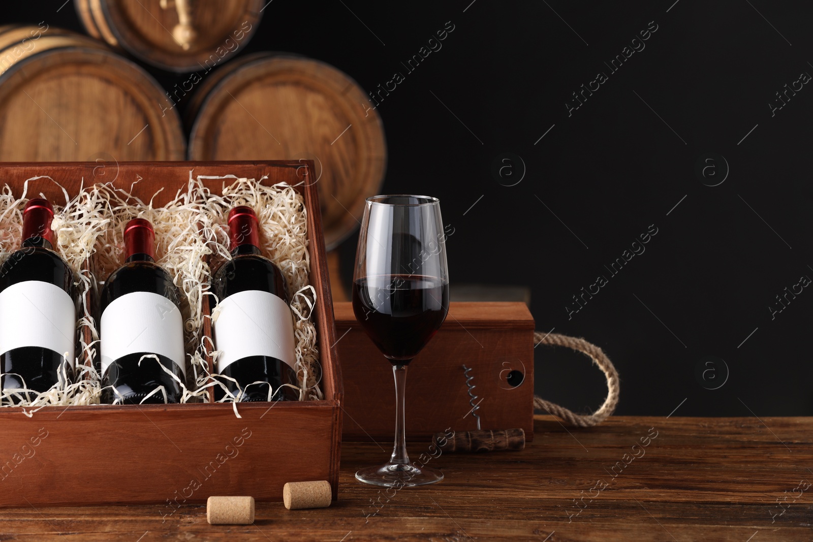 Photo of Wooden boxes, glass, corkscrew and wine bottles on table against dark background. Space for text