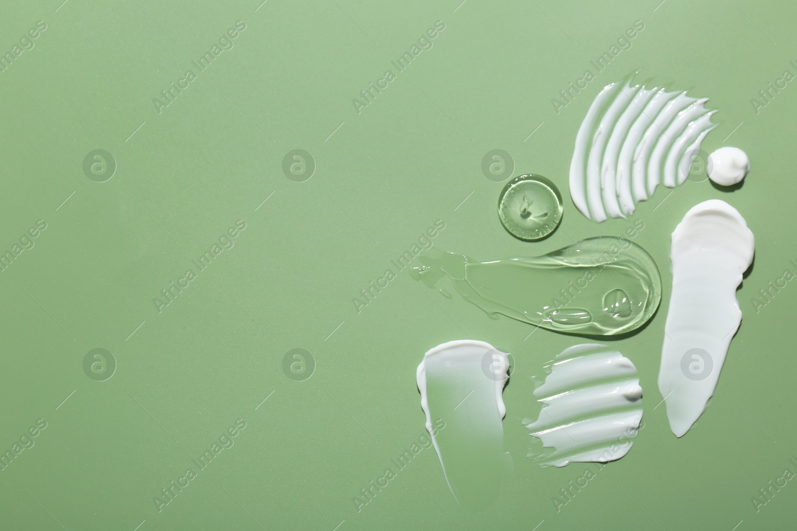 Photo of Samples of face cream on green background, top view. Space for text