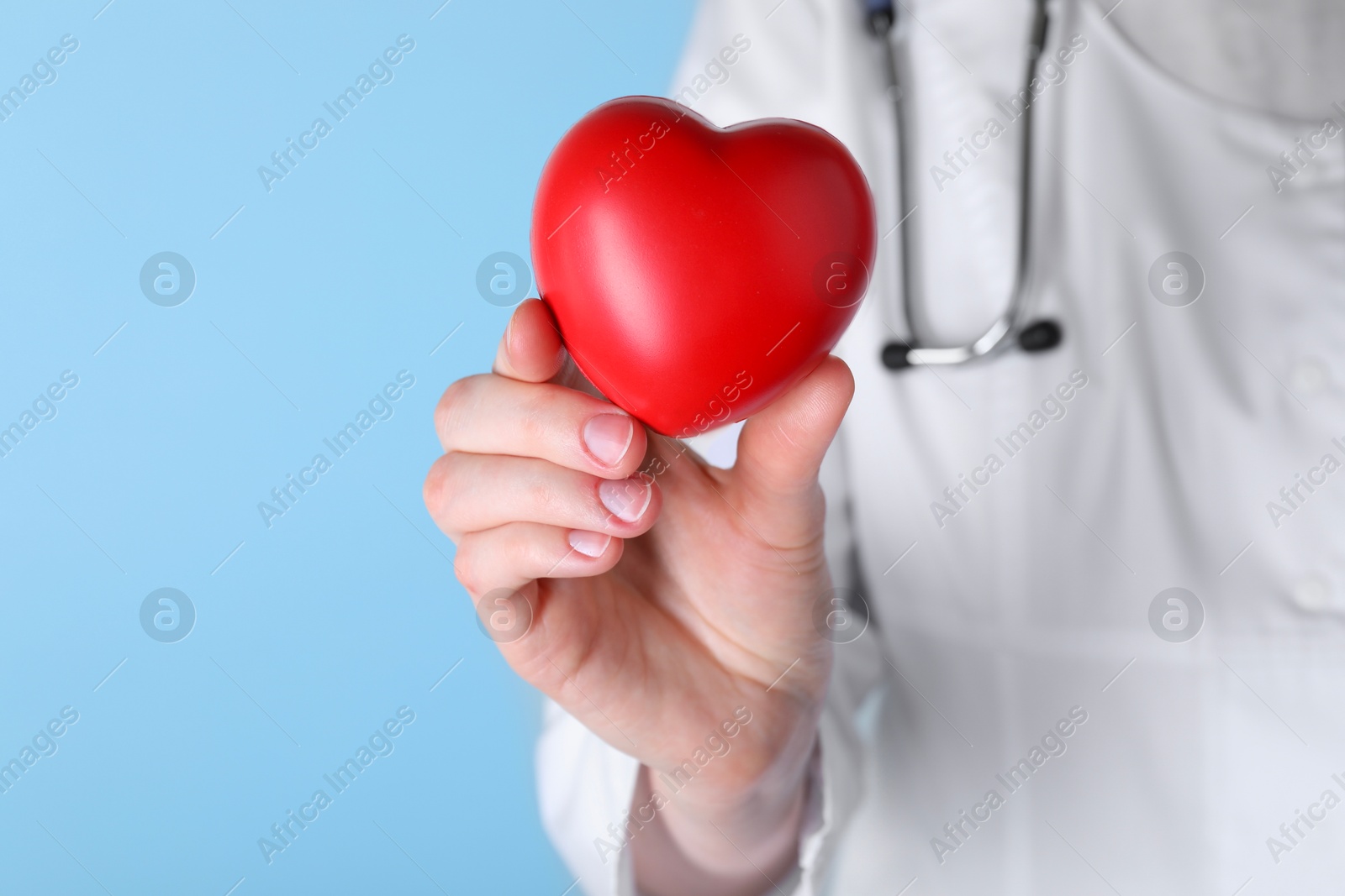 Photo of Doctor with red heart on light blue background, closeup. Space for text