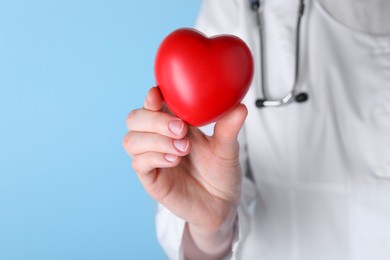Photo of Doctor with red heart on light blue background, closeup. Space for text