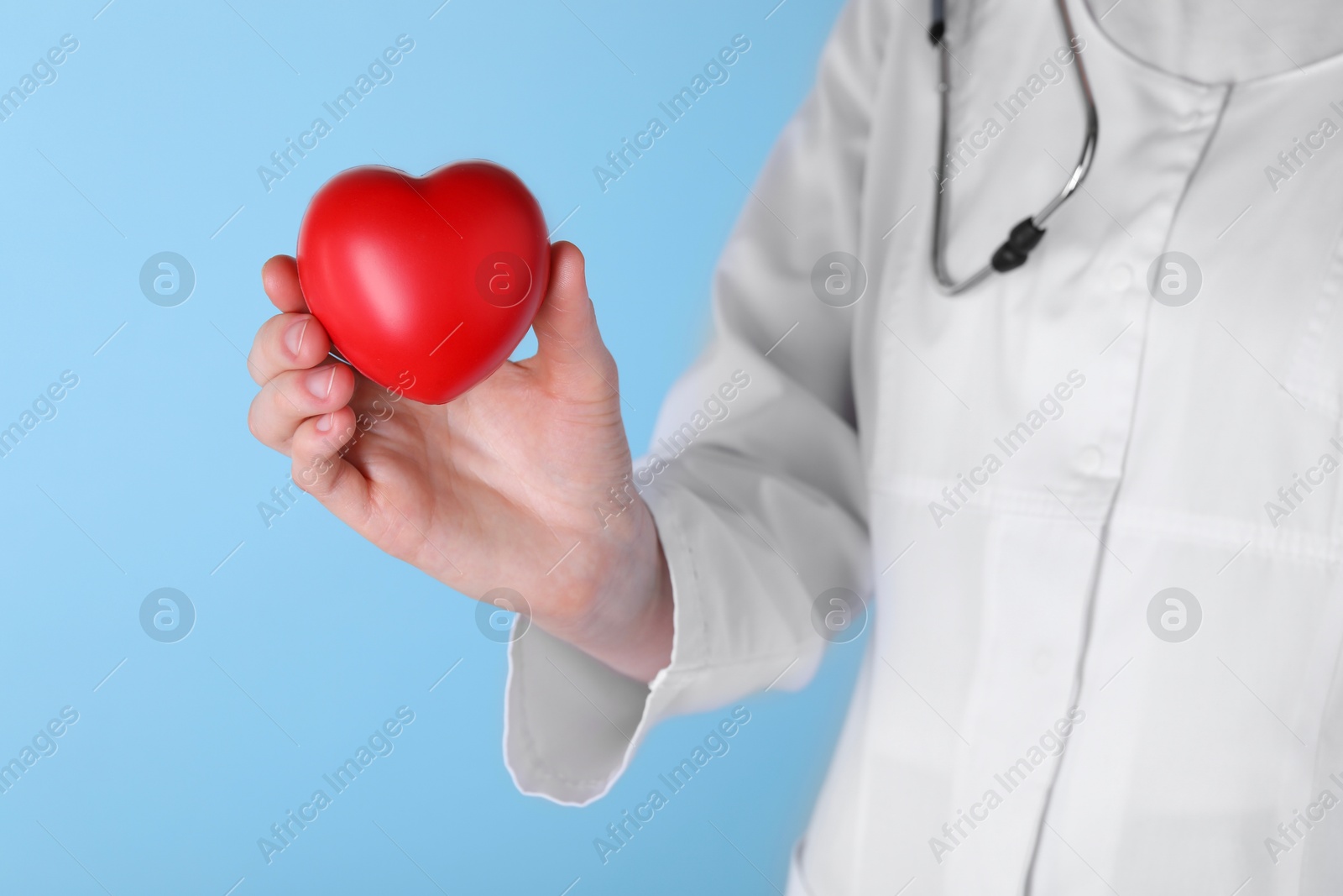 Photo of Doctor with red heart on light blue background, closeup