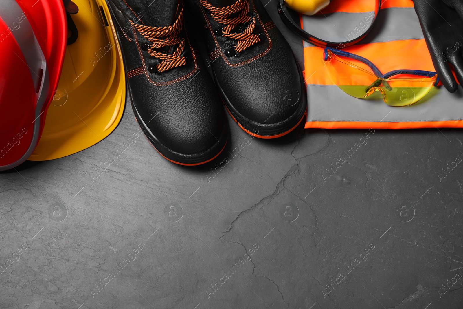 Photo of Pair of working boots, hard hats and other personal protective equipment on black surface, flat lay. Space for text