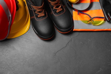 Photo of Pair of working boots, hard hats and other personal protective equipment on black surface, flat lay. Space for text
