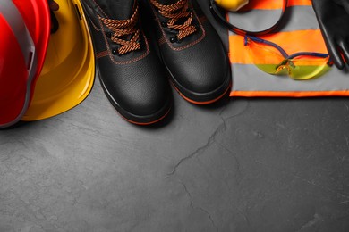 Pair of working boots, hard hats and other personal protective equipment on black surface, flat lay. Space for text