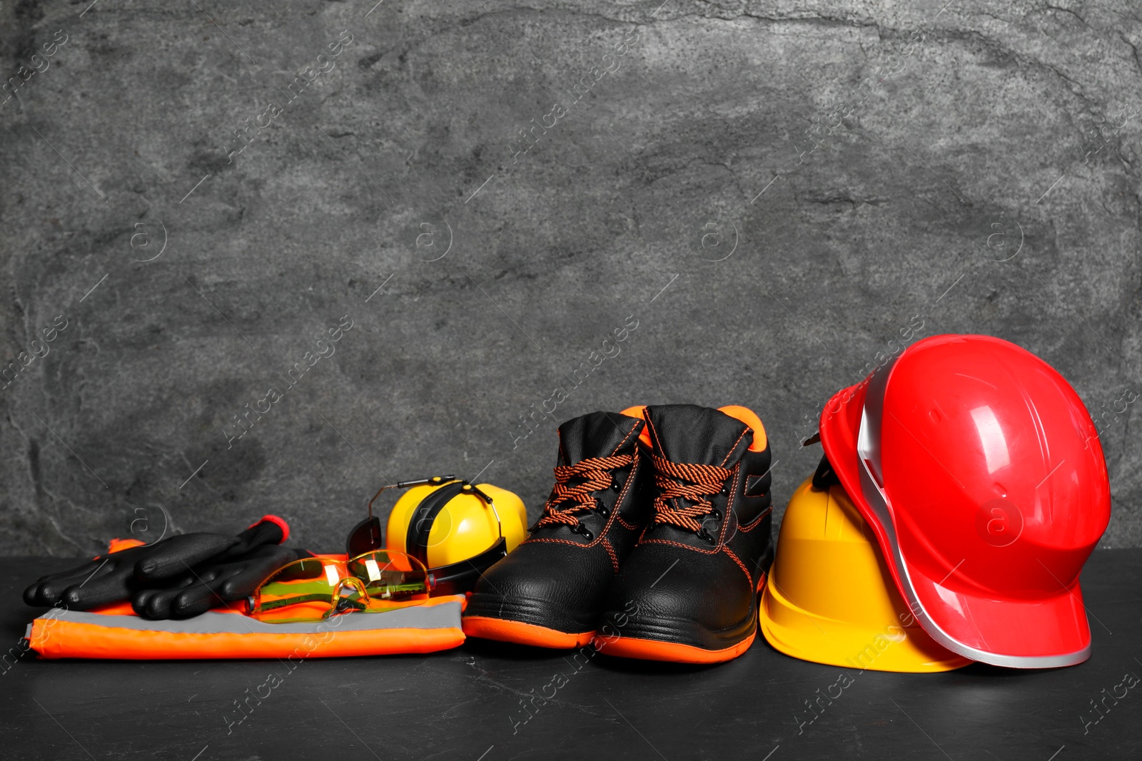 Photo of Pair of working boots, hard hats and other personal protective equipment on black surface