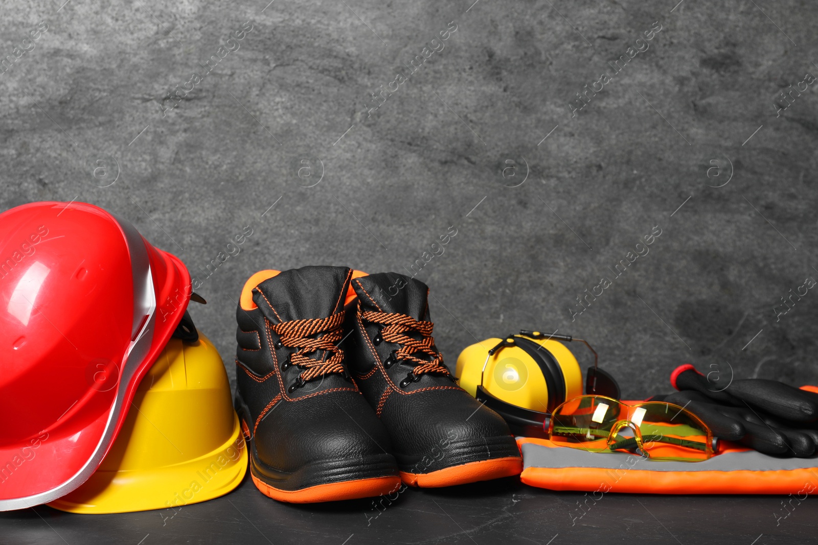Photo of Pair of working boots, hard hats and other personal protective equipment on black surface