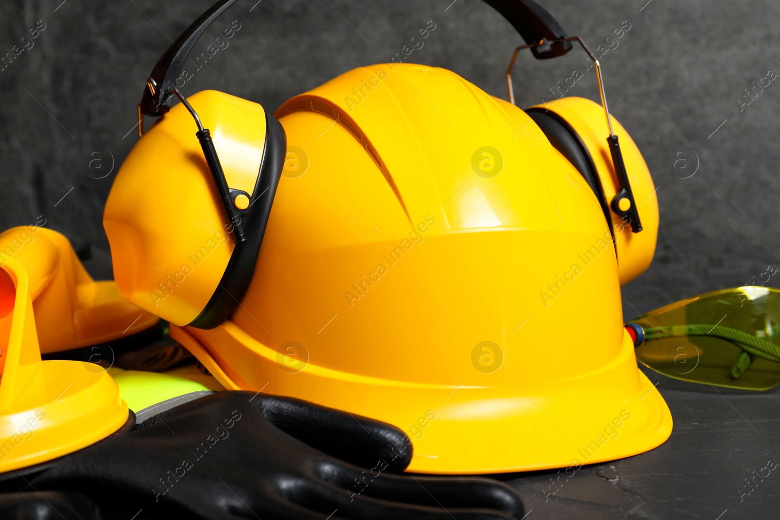 Photo of Yellow hard hat, earmuffs and other personal protective equipment on black surface, closeup