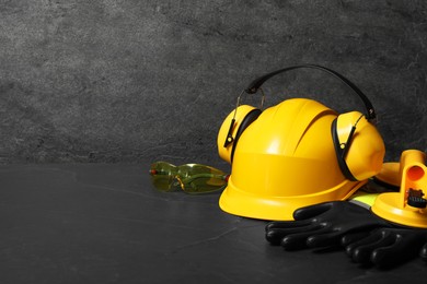 Photo of Yellow hard hat, earmuffs and other personal protective equipment on black surface. Space for text