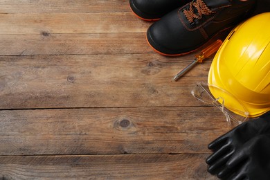 Photo of Pair of working boots, hard hat, protective gloves, goggles and screwdriver on wooden surface, flat lay. Space for text