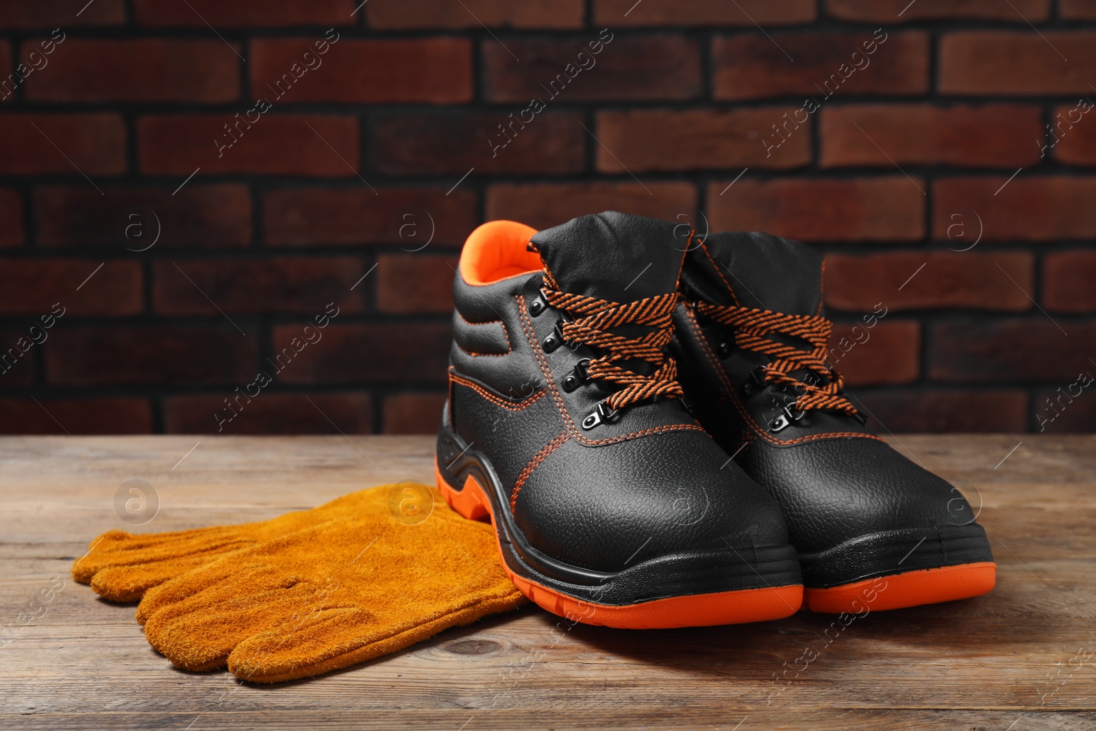 Photo of Pair of working boots and protective gloves on wooden surface