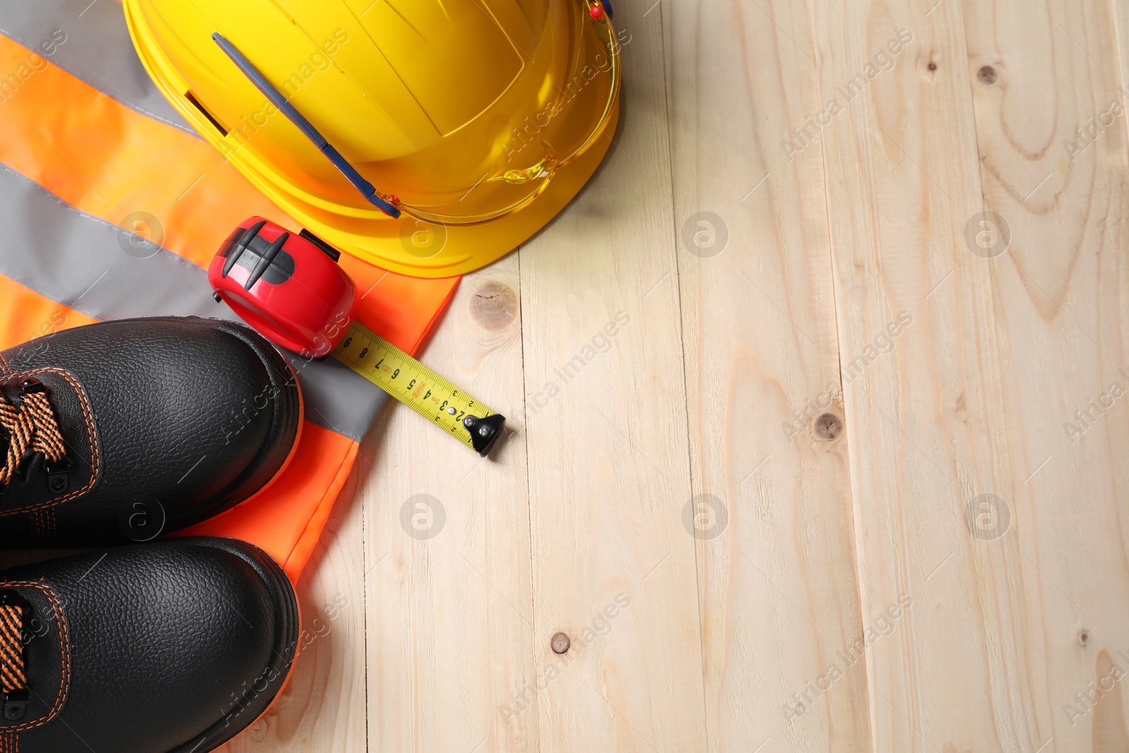 Photo of Pair of working boots, hard hat and tape measure on wooden surface, top view. Space for text