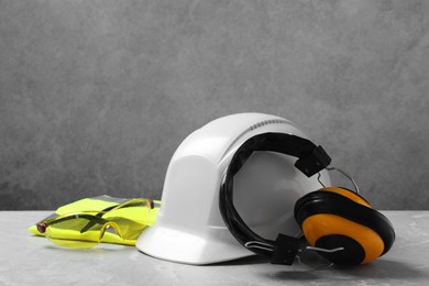 Photo of Hard hat, reflective vest, googles and earmuffs on grey surface