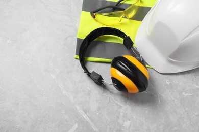 Photo of Hard hat, reflective vest, googles and earmuffs on grey surface, top view. Space for text