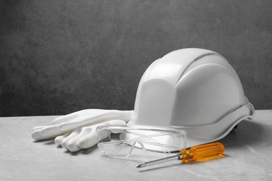 Photo of Hard hat, protective gloves, goggles and screwdriver on grey surface. Space for text