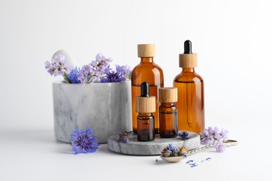 Photo of Aromatherapy. Different essential oils, flowers, mortar and pestle on white background