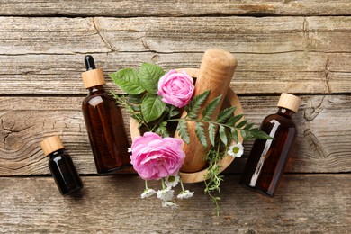 Aromatherapy. Different essential oils, flowers, mortar and pestle on wooden table, flat lay