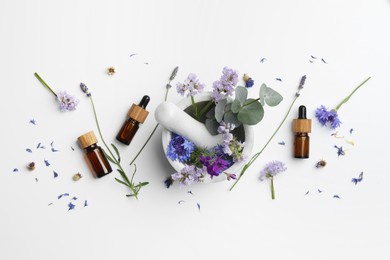 Photo of Aromatherapy. Essential oils, flowers, eucalyptus leaves, mortar and pestle on white background, flat lay