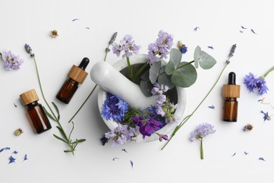 Photo of Aromatherapy. Essential oils, flowers, eucalyptus leaves, mortar and pestle on white background, flat lay