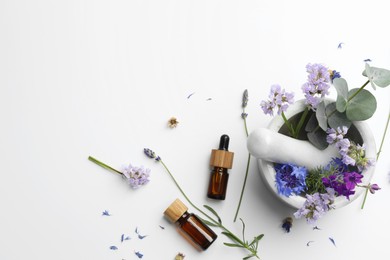 Photo of Aromatherapy. Essential oils, flowers, eucalyptus leaves, mortar and pestle on white background, flat lay. Space for text