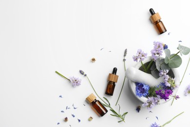 Photo of Aromatherapy. Essential oils, flowers, eucalyptus leaves, mortar and pestle on white background, flat lay. Space for text