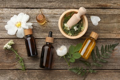 Aromatherapy. Different essential oils, flowers, green leaves, mortar and pestle on wooden table, flat lay