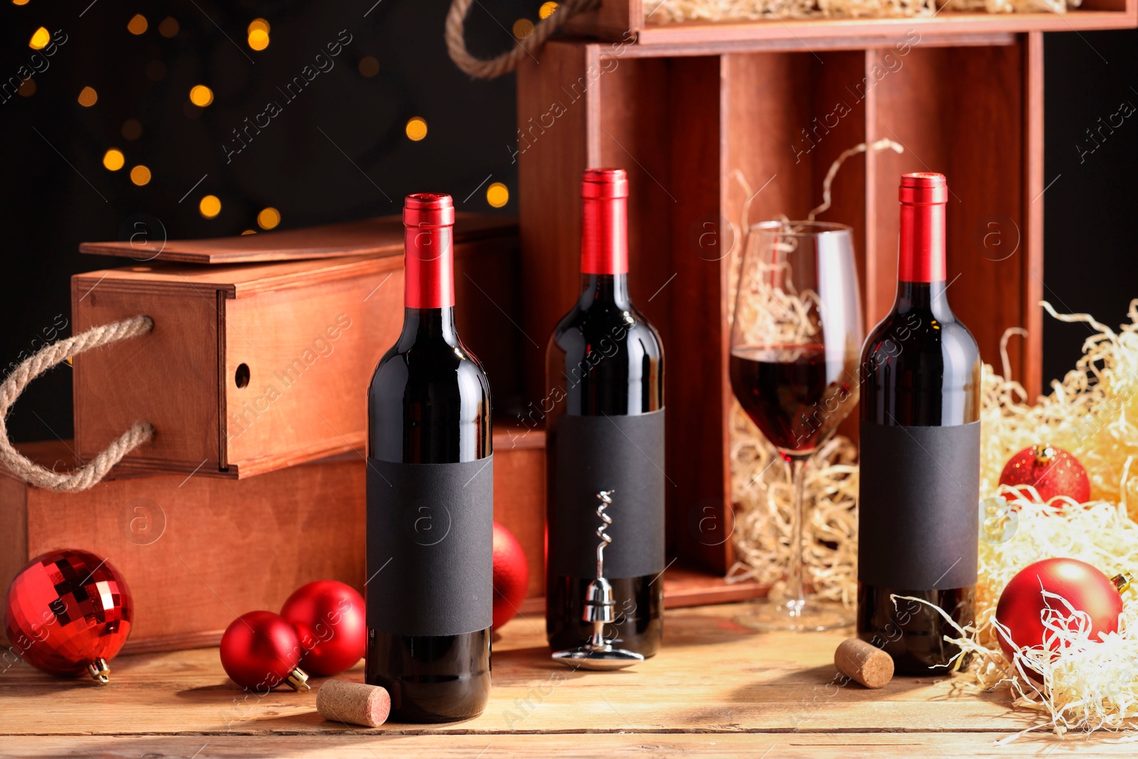 Photo of Bottles of wine, glass, wooden boxes, corks and red Christmas balls on table