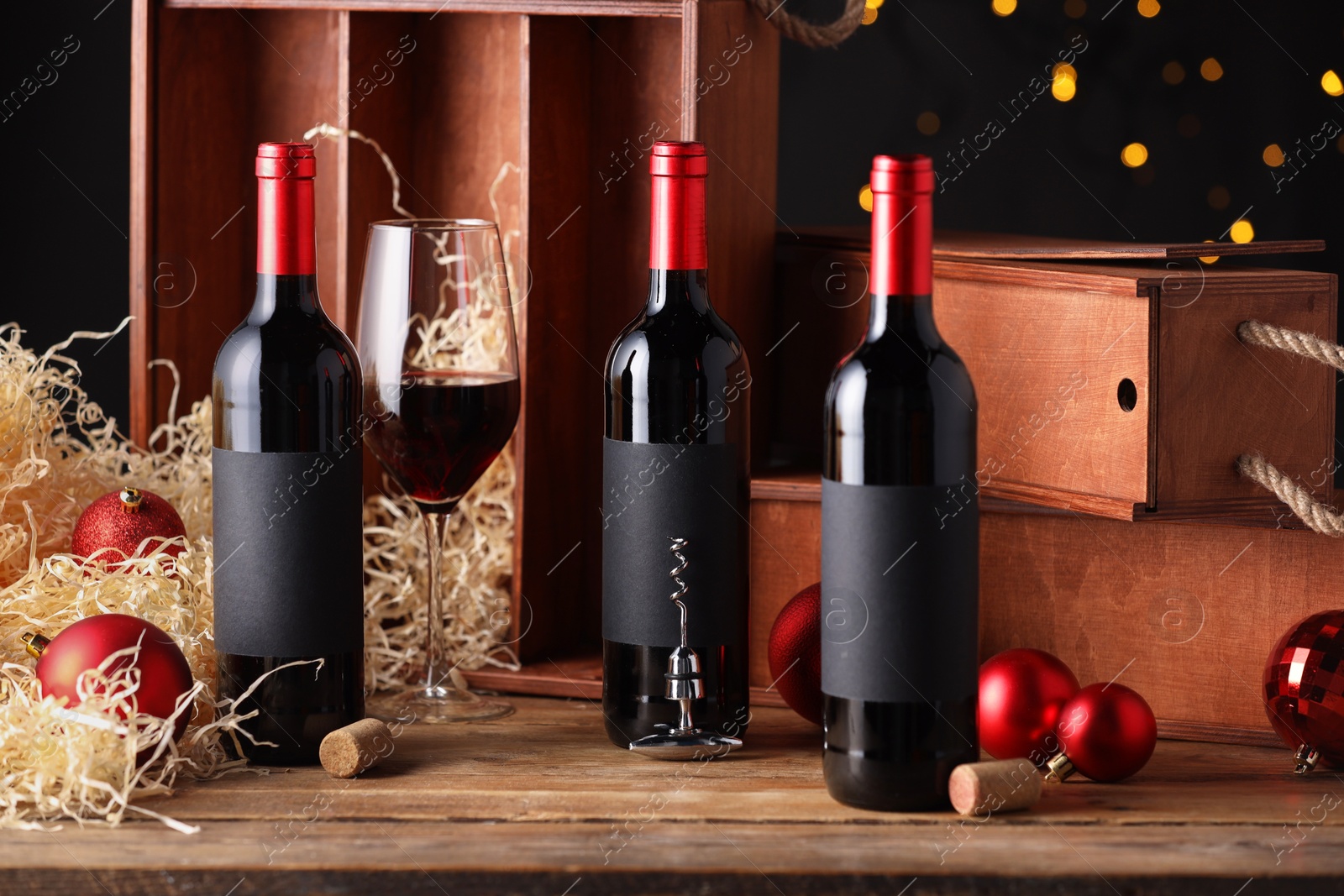 Photo of Bottles of wine, glass, wooden boxes, corks and red Christmas balls on table