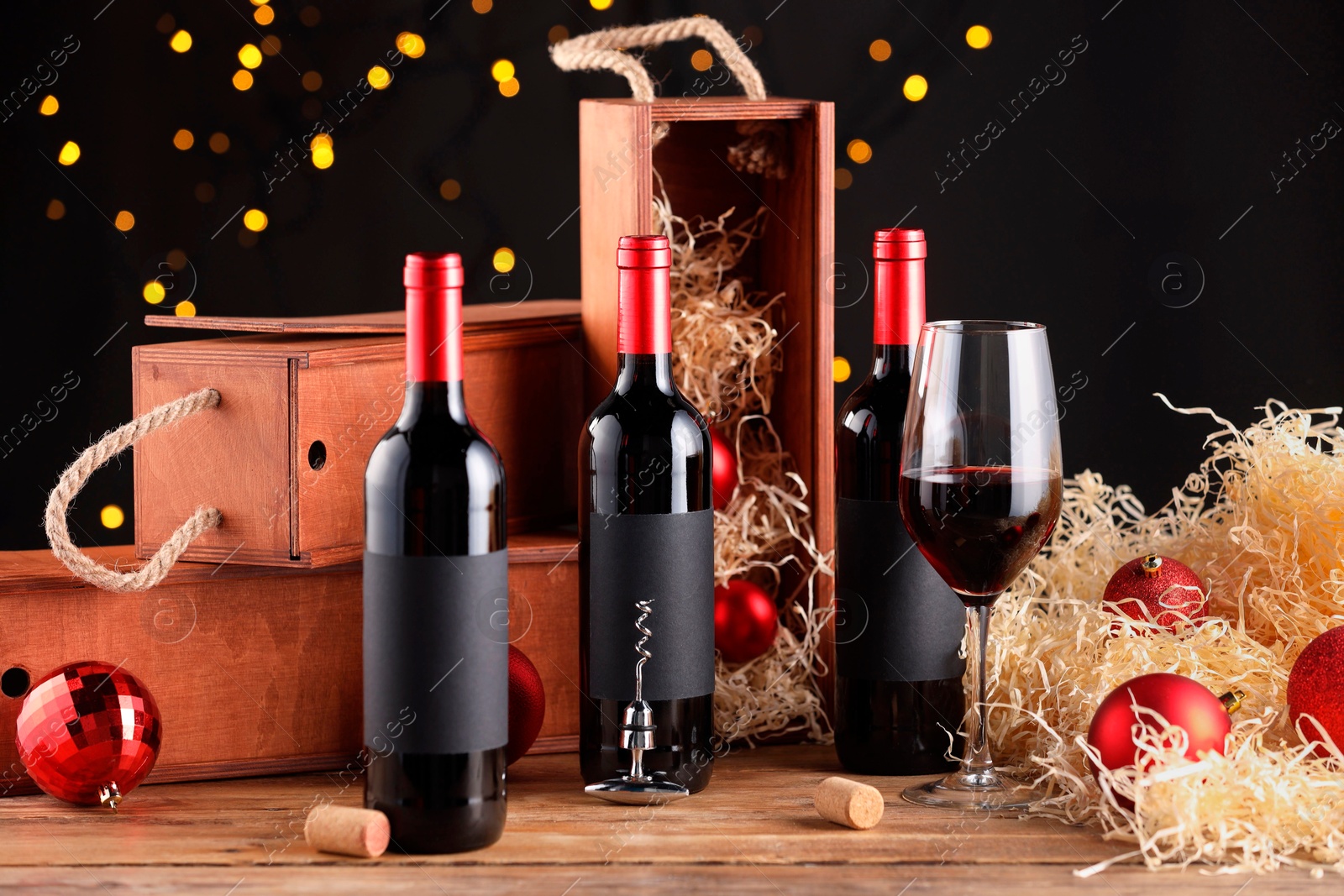 Photo of Bottles of wine, glass, wooden boxes, corks and red Christmas balls on table