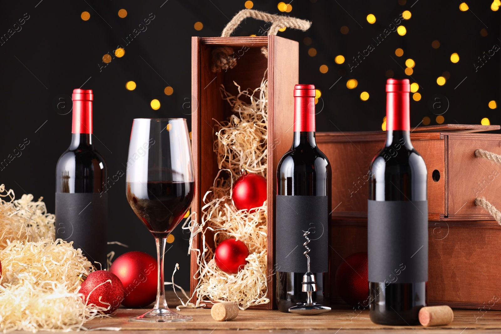 Photo of Bottles of wine, glass, wooden boxes, corks and red Christmas balls on table