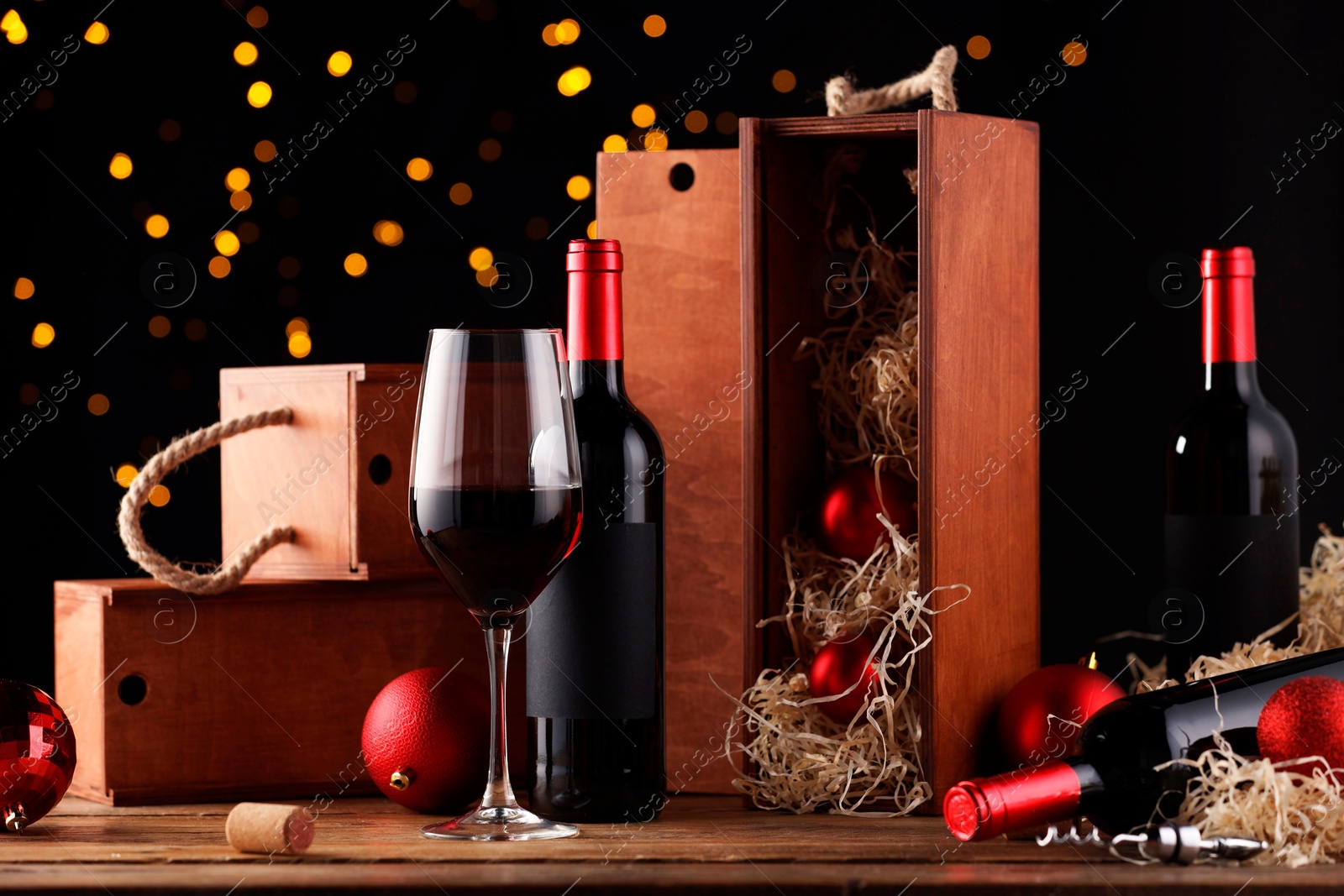 Photo of Bottles of wine, glass, wooden boxes, corkscrew and red Christmas balls on table