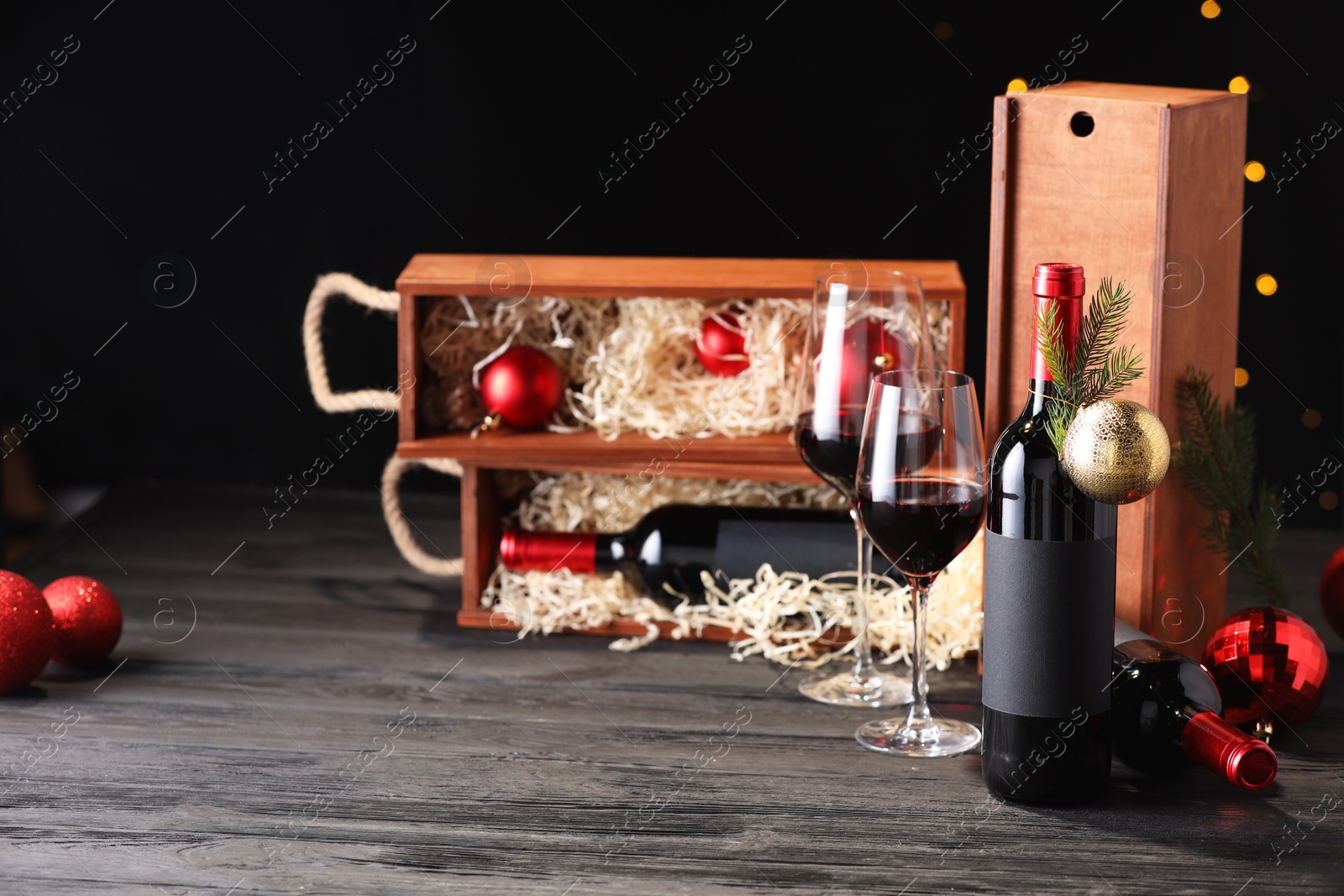 Photo of Bottles of wine, glasses, wooden boxes, fir twigs and Christmas balls on table